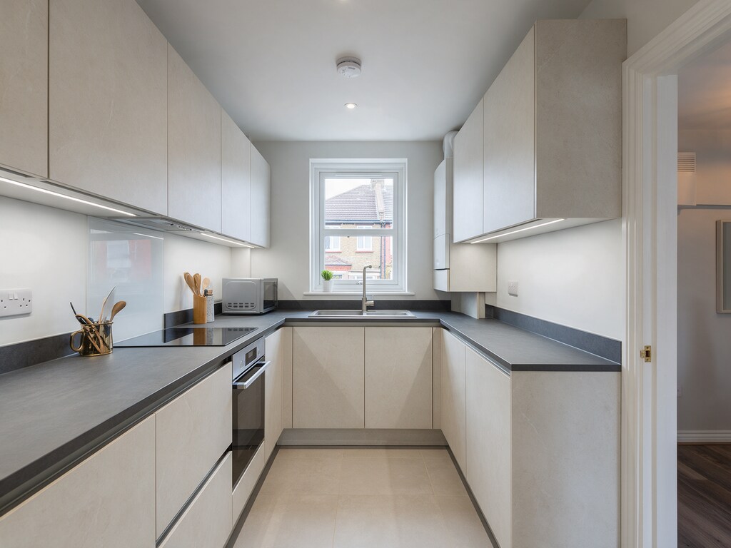 Compact stone-coloured handleless galley kitchen in Romford